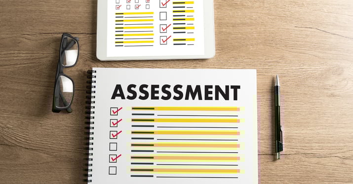 A picture of black folded glasses on a table next to a clipboard that reads Assessment and has checked boxes with red check marks on it