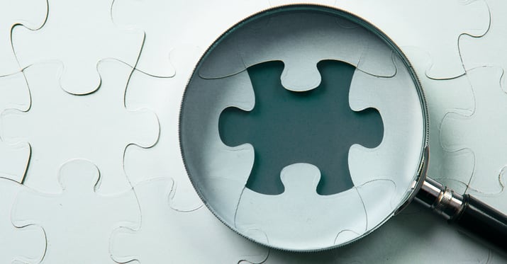 A magnifying glass hovering over a space where a puzzle piece is missing from a puzzle